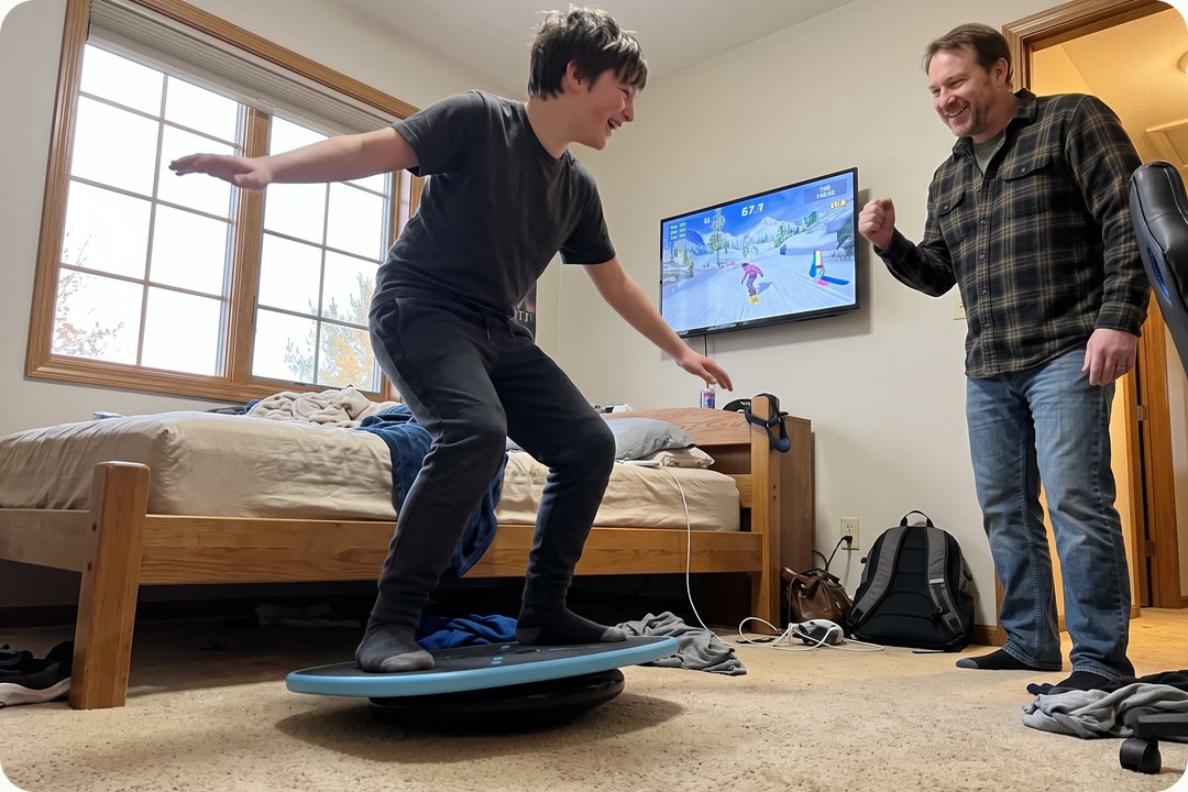 A teen on GoBalance in front of the TV while his dad cheers